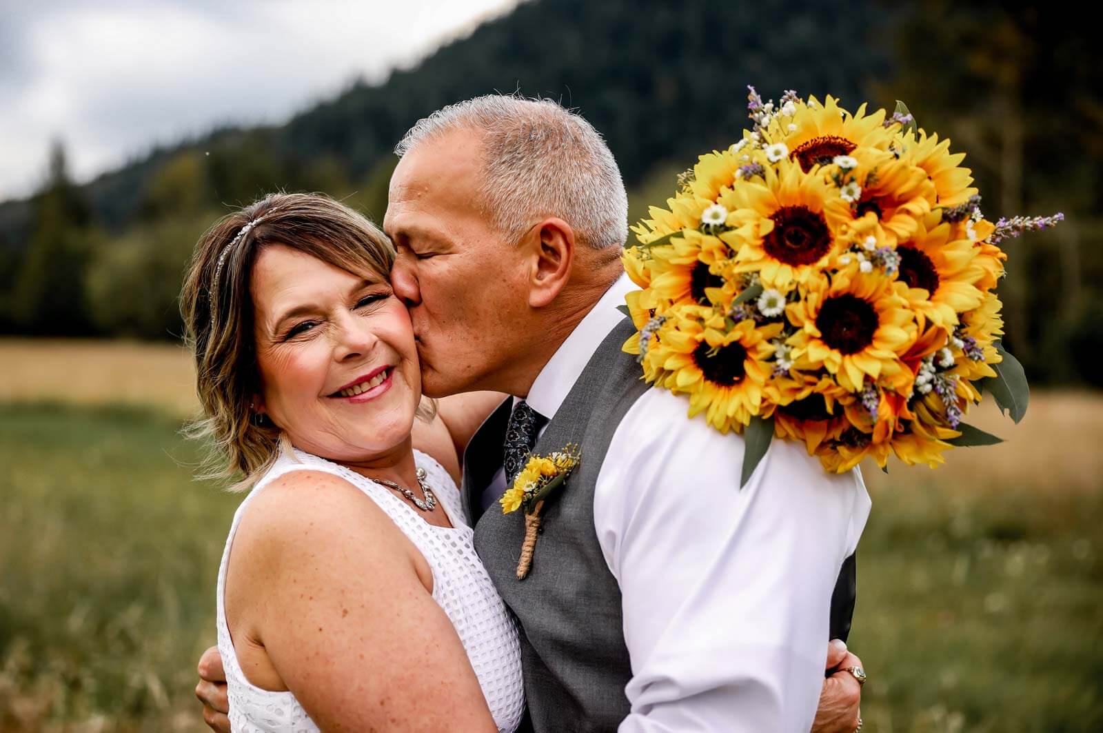 Bride and groom kiss with sunflower bouquet