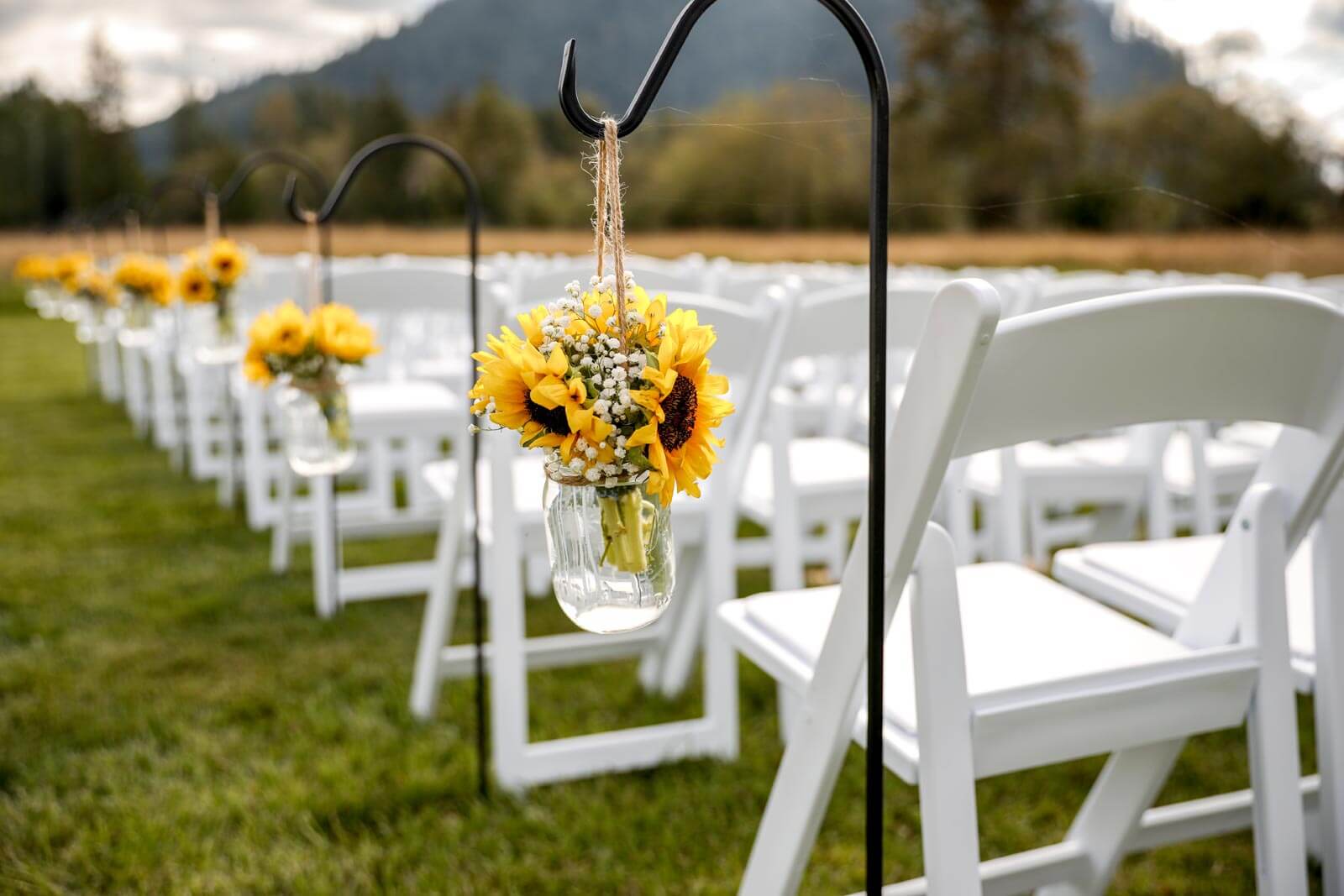 Wedding ceremony aisle with shepherd hooks holding mason jars with sunflower bouquets
