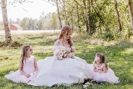 Bride with flowergirls sitting in grass at Mount Peak Farm wedding venue