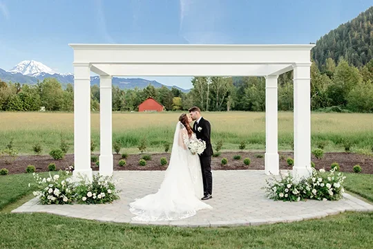 Bride and groom kissing under white arbor with Mount Rainier views at Mount Peak Farm ceremony area.
